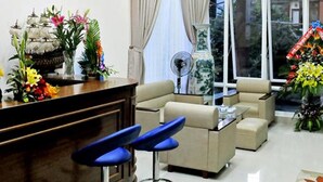 Una sala moderna con una lámpara redonda en el techo, un sofá, dos taburetes de bar, un jarrón decorativo y una ventana con cortinas.