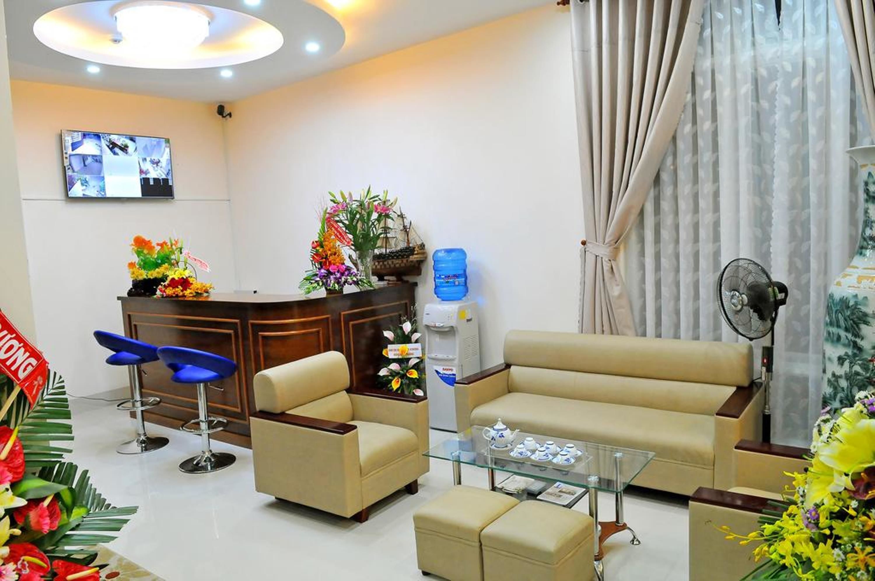 A modern reception area with a sofa, two chairs, a coffee table, a water dispenser, and a TV mounted on the wall.