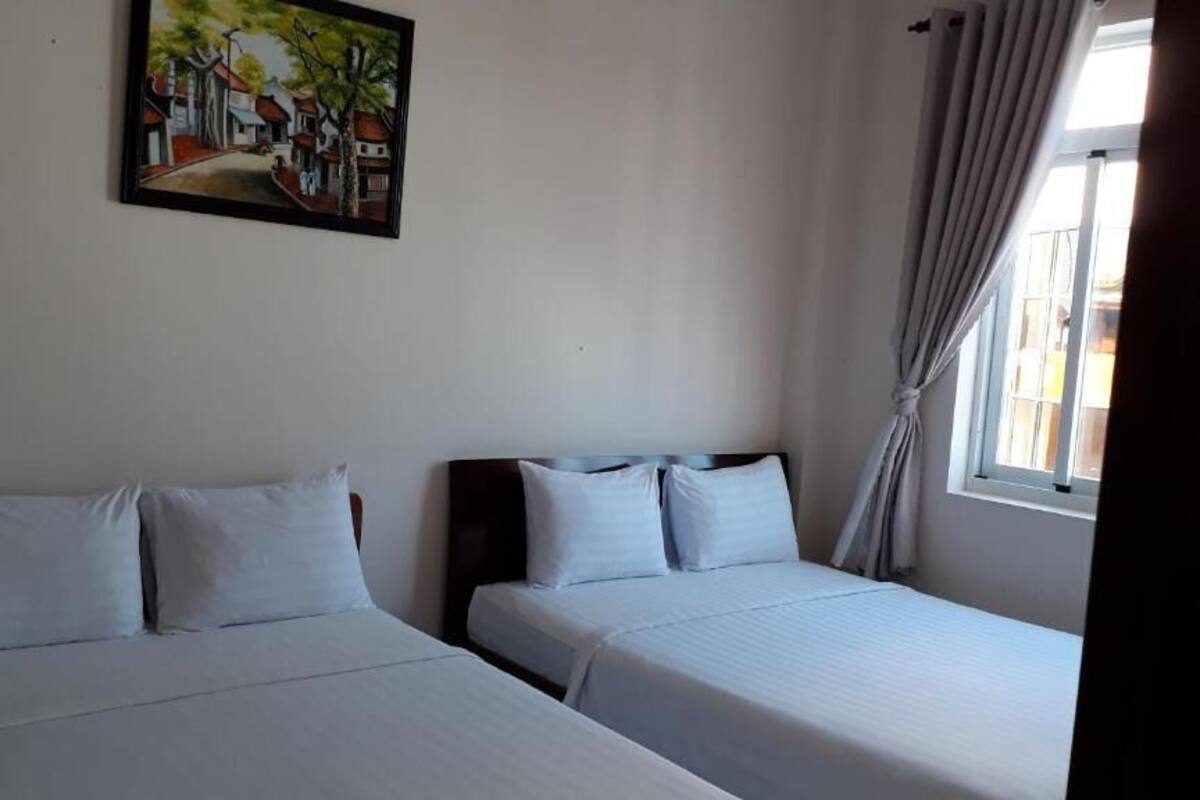 Ein Hotelzimmer mit zwei Betten, einem Bild an der Wand und einem Fenster mit Vorhängen.