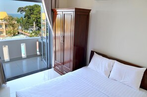 A hotel room with a bed, a wooden wardrobe, and a balcony with a view of buildings and trees. - Lotus Apartment Hotel (Ho Chi Minh City)