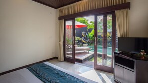 Une chambre avec un lit, une télévision et une porte-fenêtre coulissante donnant sur une zone abritant une piscine.