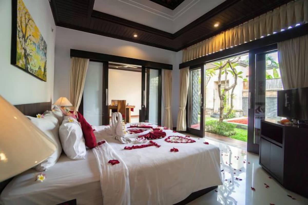 A hotel room with a large bed, a television, and a view of a garden through a sliding door.