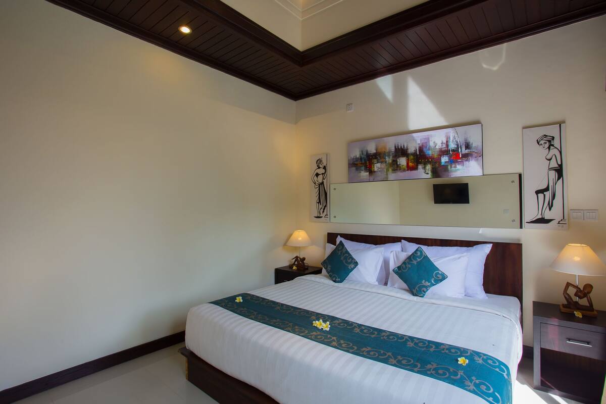 A hotel room with a large bed, two bedside tables, a flat-screen TV, and artwork on the walls.