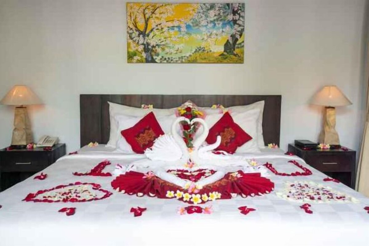 A bed with a swan design, red pillows, and a painting above.