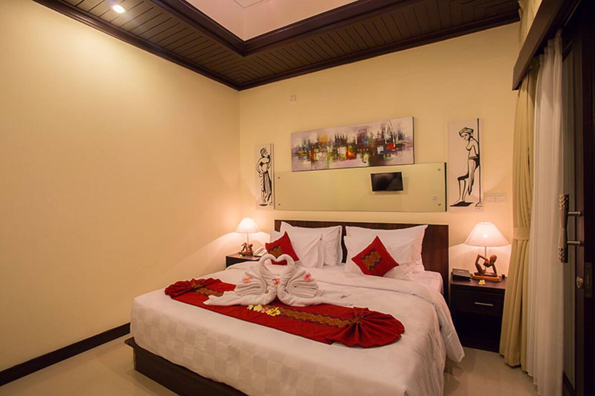 A hotel room with a large bed, two bedside tables with lamps, a painting on the wall, and a red decorative item on the bed.