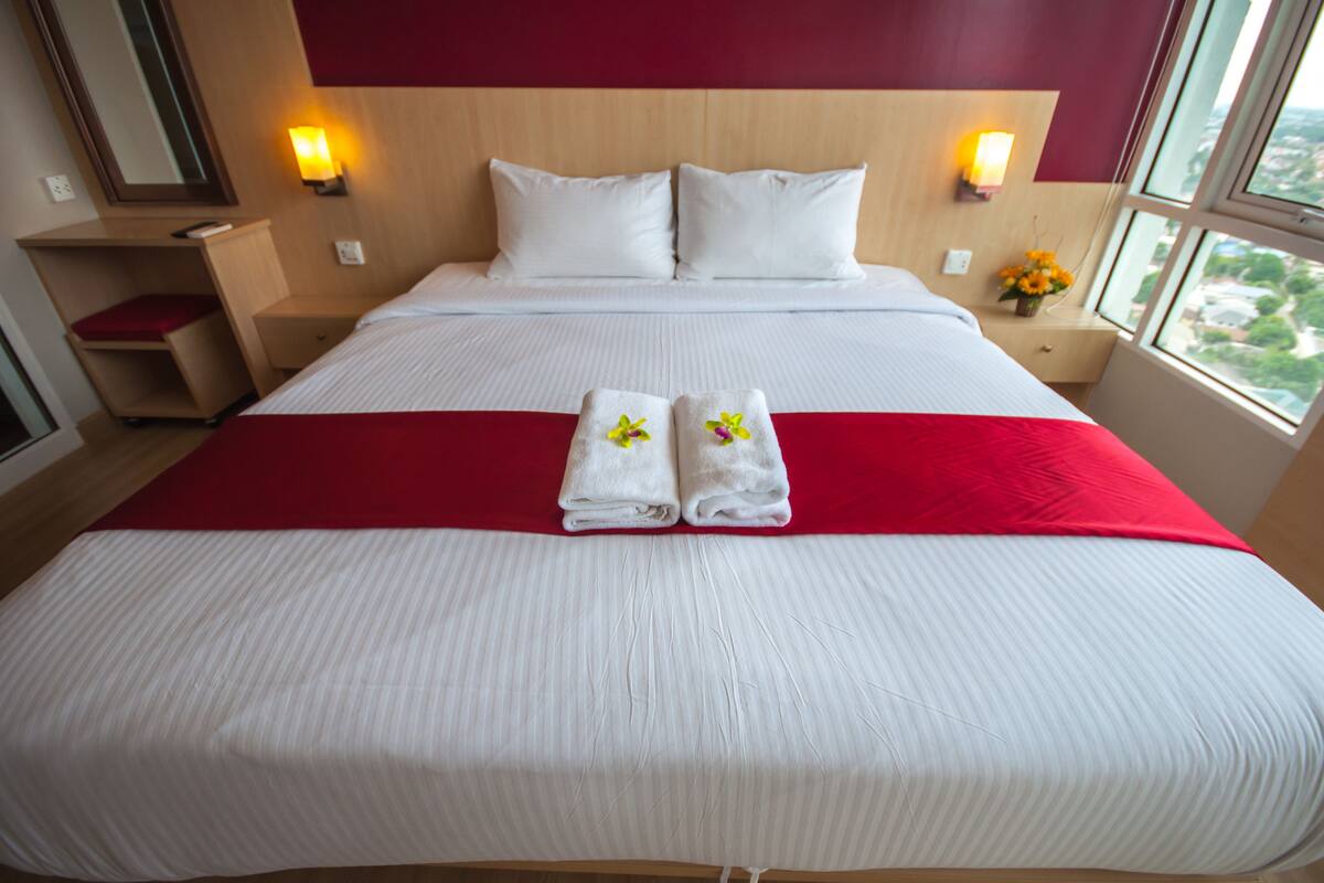 Una cama bien hecha con sábanas blancas, dos almohadas y un detalle rojo.