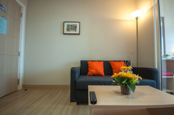 Una sala de estar con un sofá, un control remoto, un jarrón con flores y un cuadro en la pared.