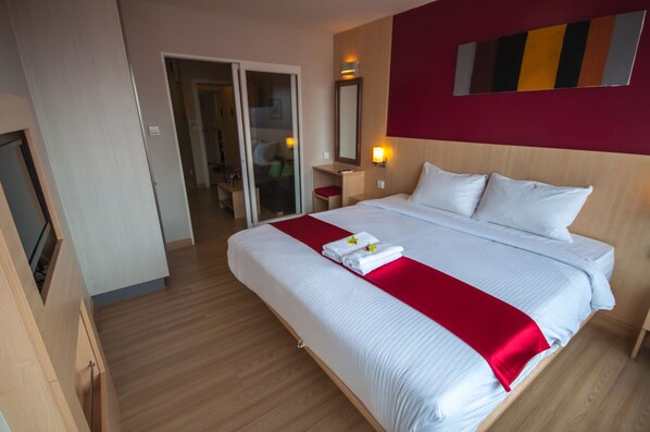Una habitación de hotel con una cama grande, una manta roja, un espejo y suelo de madera.
