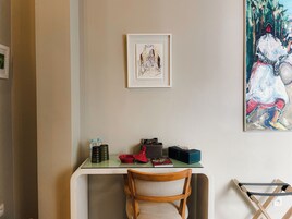 Una habitación con un escritorio de superficie de vidrio, una silla, una obra de arte enmarcada y un cuadro grande en la pared.