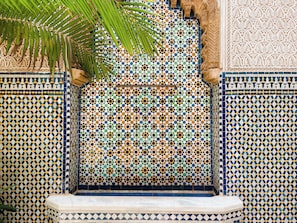 A tiled wall with geometric patterns, a bench, and a palm tree.