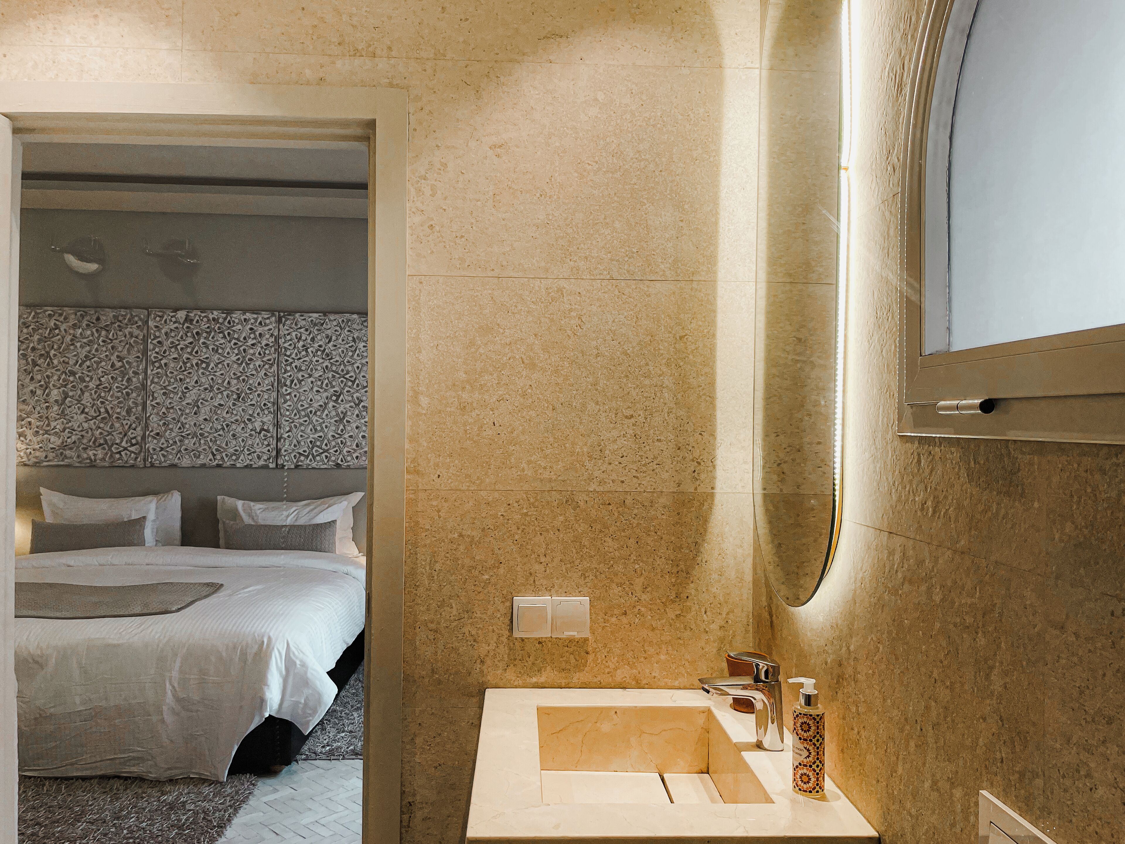A modern hotel room with a large bed, a bathroom with a marble sink, and a large mirror.