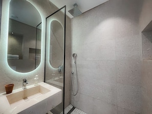 A modern bathroom with a glass shower enclosure, a sink with a mirror, and a tiled shower wall.