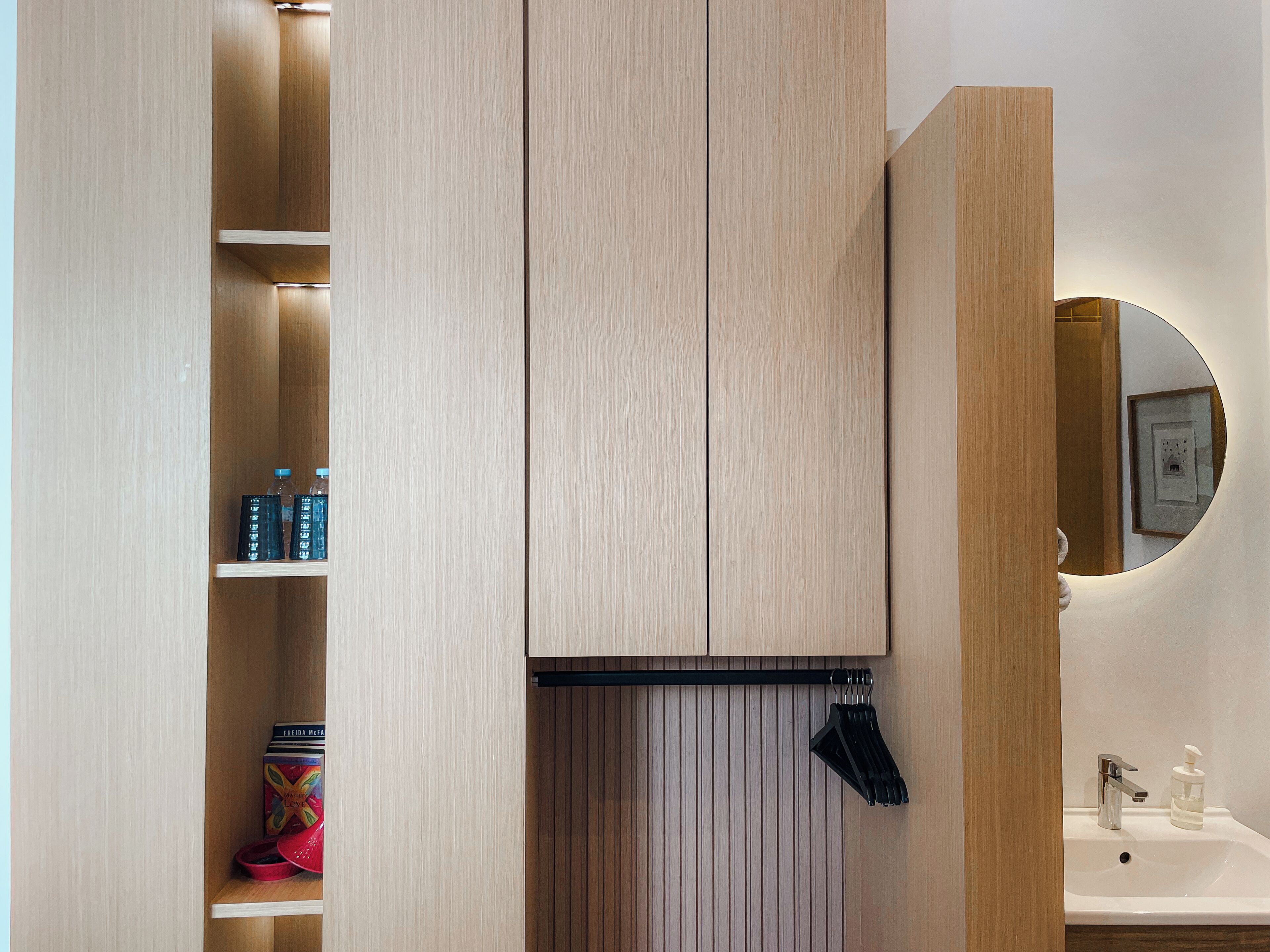 A bathroom with a wooden vanity, a mirror, a sink, and a shelf with toiletries.