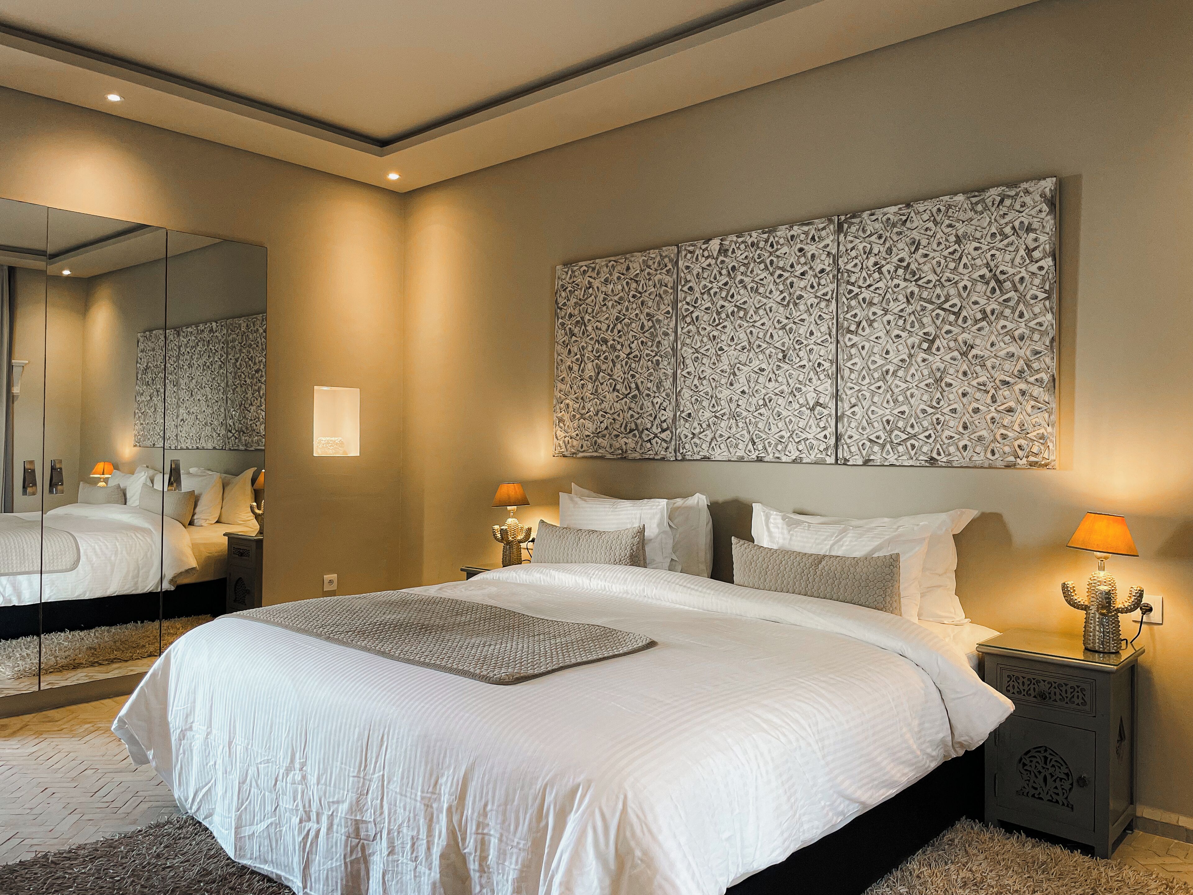Une chambre à coucher avec un grand lit, deux tables de chevet avec des lampes, une œuvre d’art accrochée au mur et un miroir.