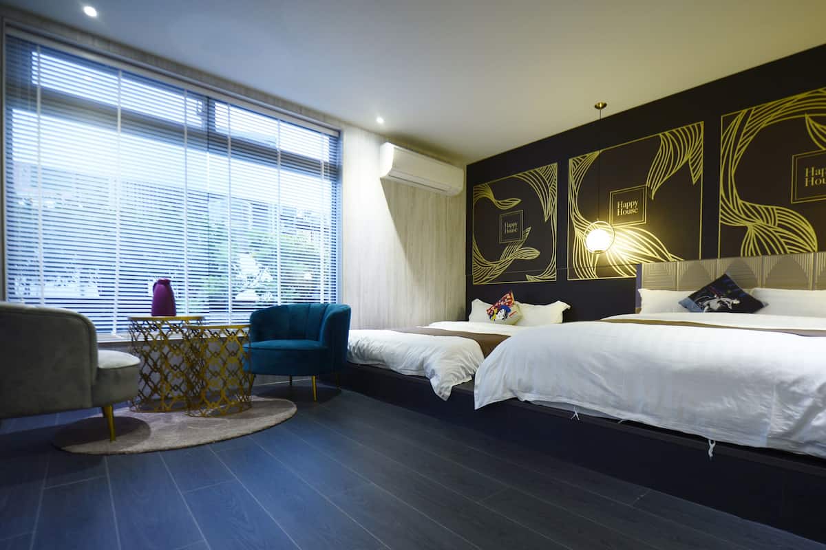 A hotel room with two beds, a desk, a chair, and a large window with blinds.