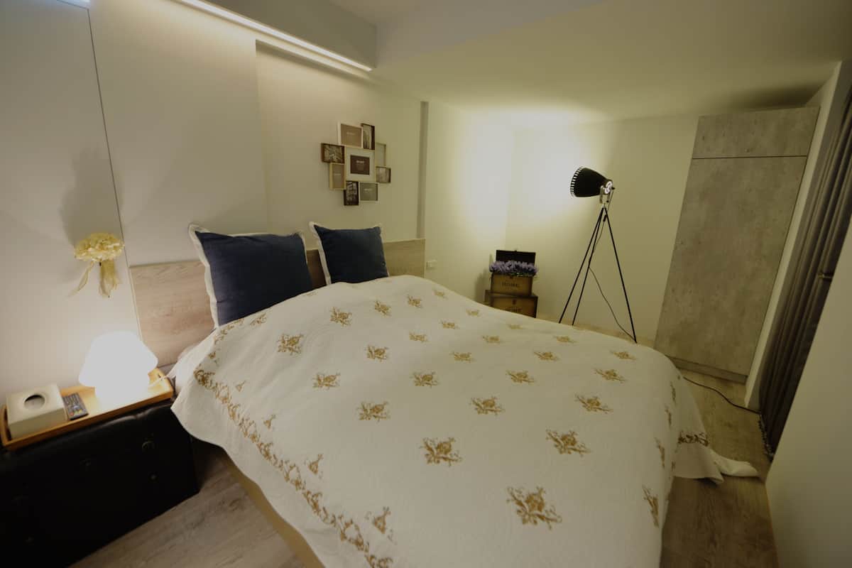 A bedroom with a bed, bedside table, lamp, and a wall-mounted picture frame.