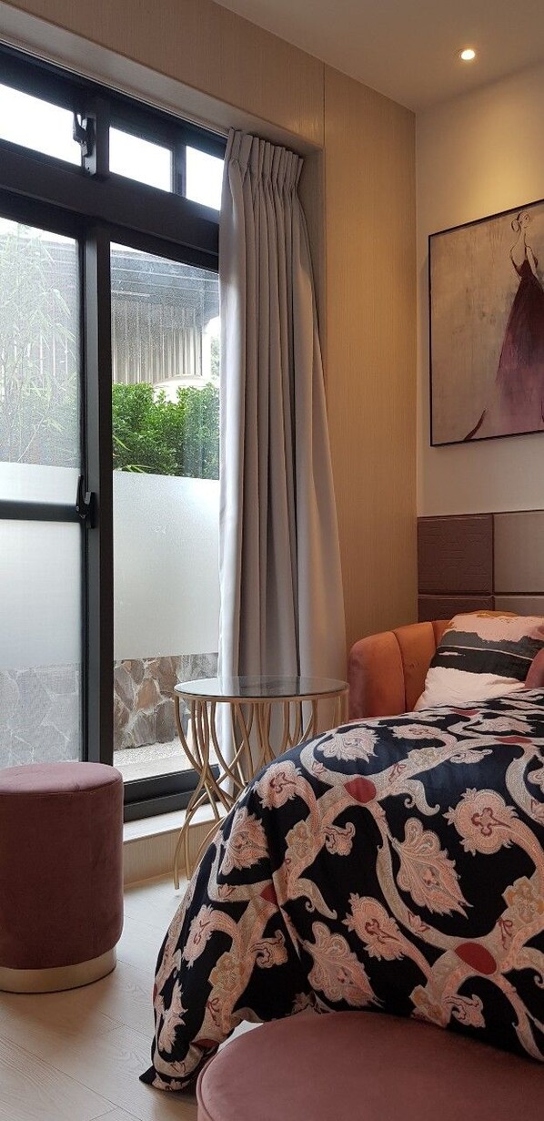 A bedroom with a bed, a window with curtains, a small table, and a painting on the wall.