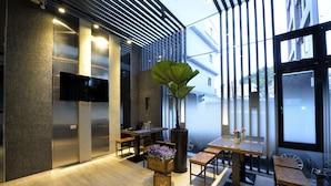 A modern interior with a wooden floor, metal-framed tables and benches, a large potted plant, and a flat-screen TV mounted on the wall. - Happy House B&B, Juifan (New Taipei City)