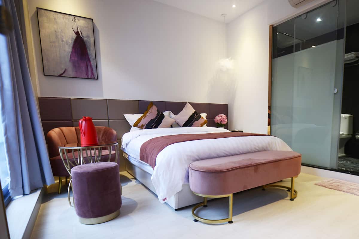 A modern bedroom with a large bed, a glass shower enclosure, and a red chair.