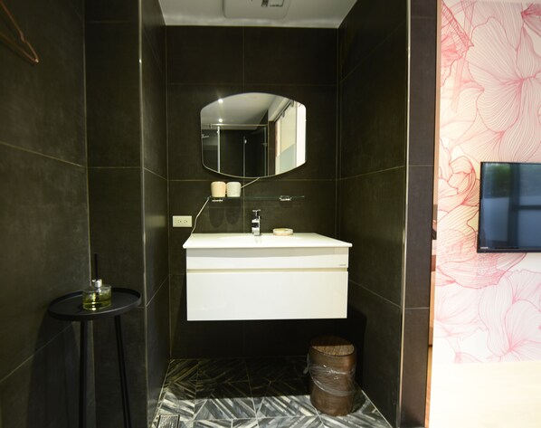 Un baño moderno con un lavamanos blanco, un espejo encima y un cubo de basura redondo pequeño.