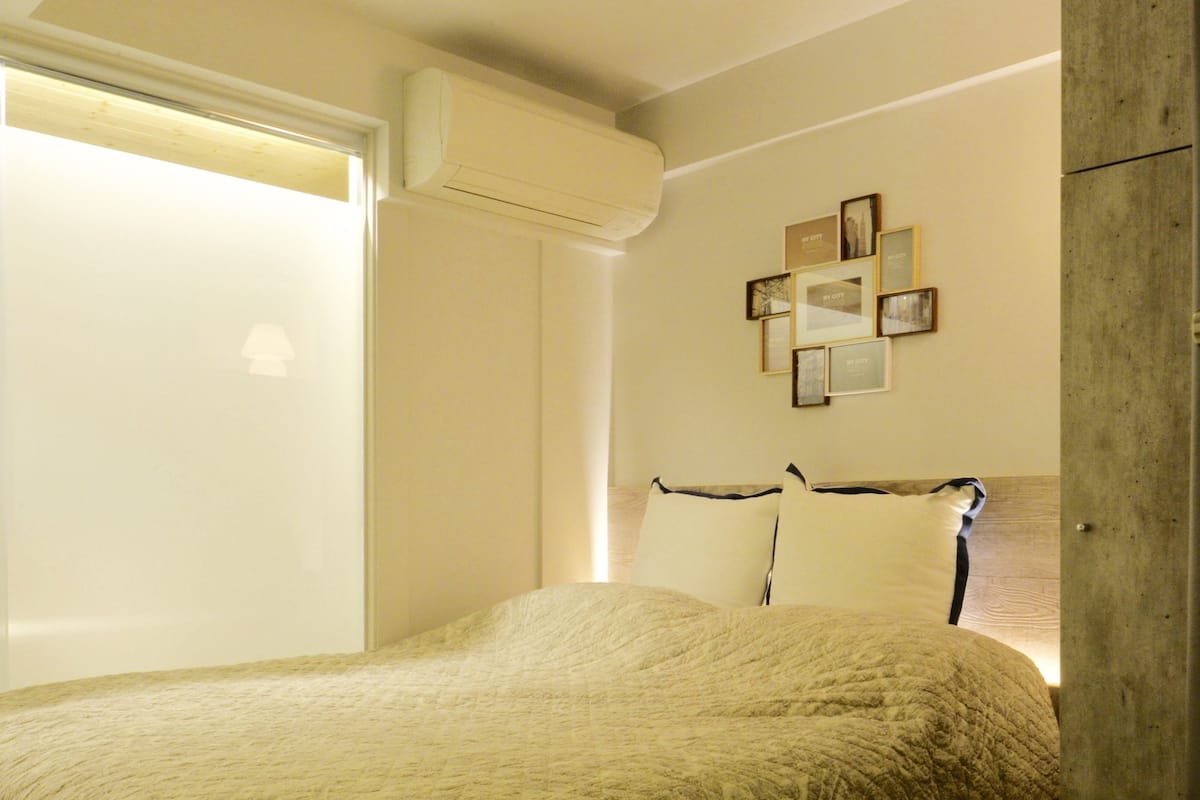 A bedroom with a bed, a wooden headboard, a wall-mounted air conditioner, and a framed picture collection.
