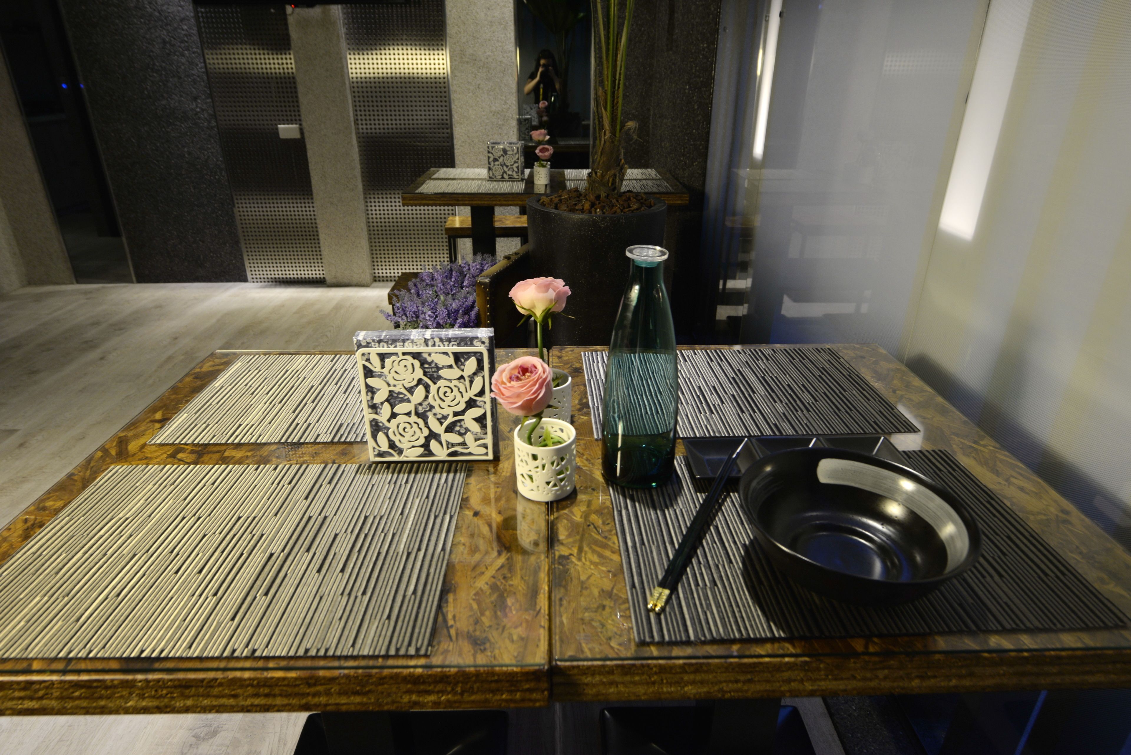 A dining table with a vase of flowers, a bottle, and a bowl.