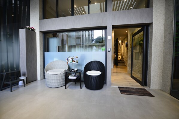 A modern entrance with a glass door, a wicker chair, a small table, and a rug.
