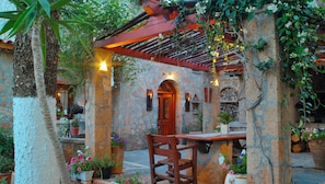 A stone-walled courtyard with a wooden pergola, potted plants, and a rustic wooden table and chair. - W Suites Annex by Estia (Hersonissos)