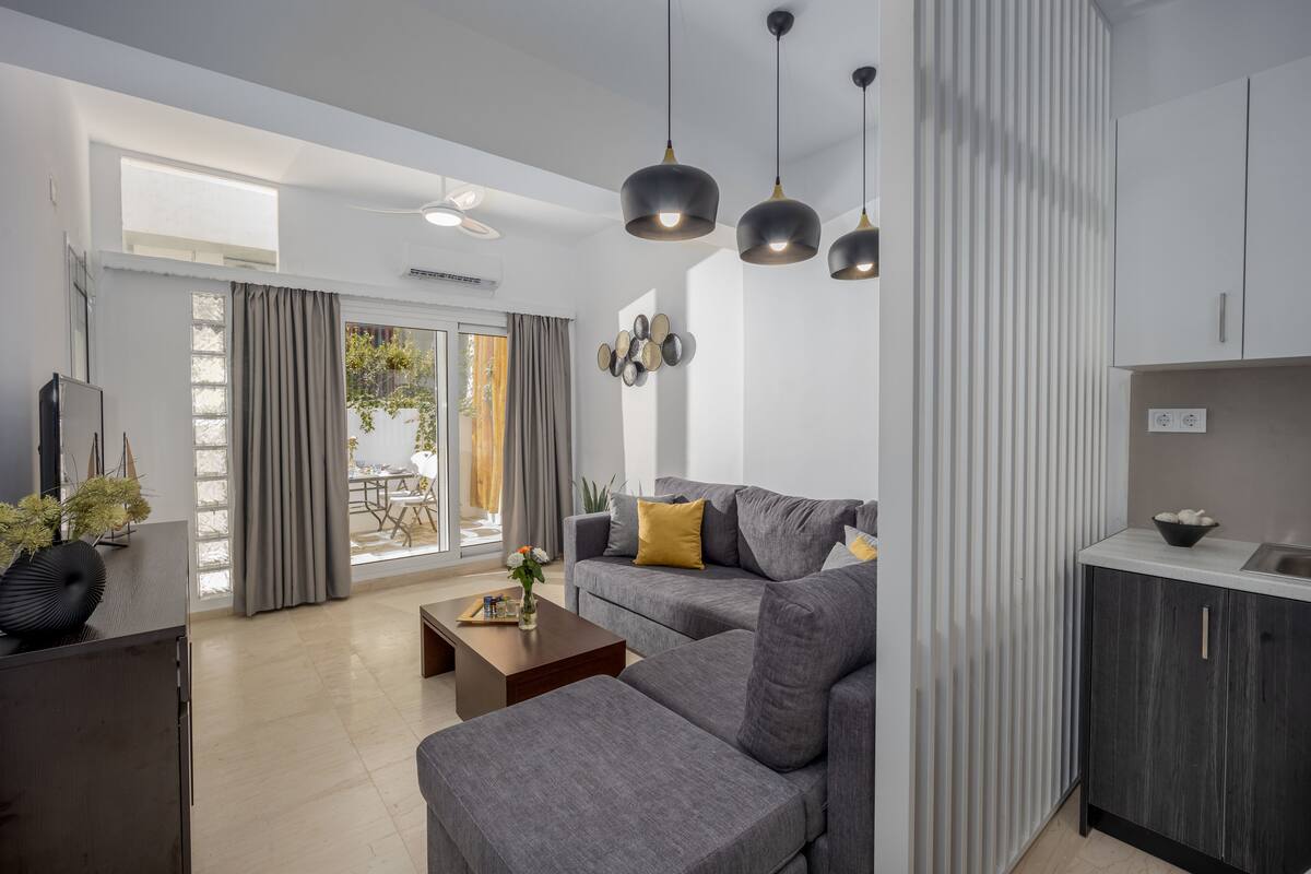 Een moderne woonkamer met een grijze bank, een salontafel en hanglampen. Er is een schuifdeur die leidt naar een balkon.