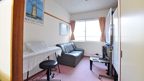Una habitación con una cama, un sofá gris, un escritorio con computadora y una ventana con cortinas.