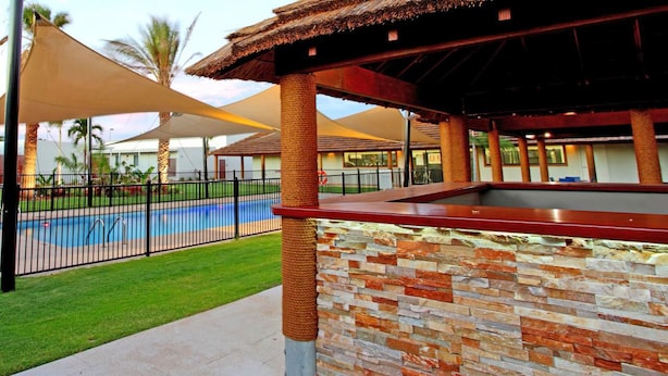 A pool area with a stone wall and a covered seating area. - Cherratta Lodge (Karratha Industrial Estate)