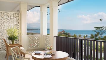 Un balcón con vista al mar, una mesa redonda de madera con sillas y un muro decorativo.