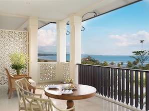 A balcony with a view of the sea, a round wooden table with chairs, and a decorative wall.