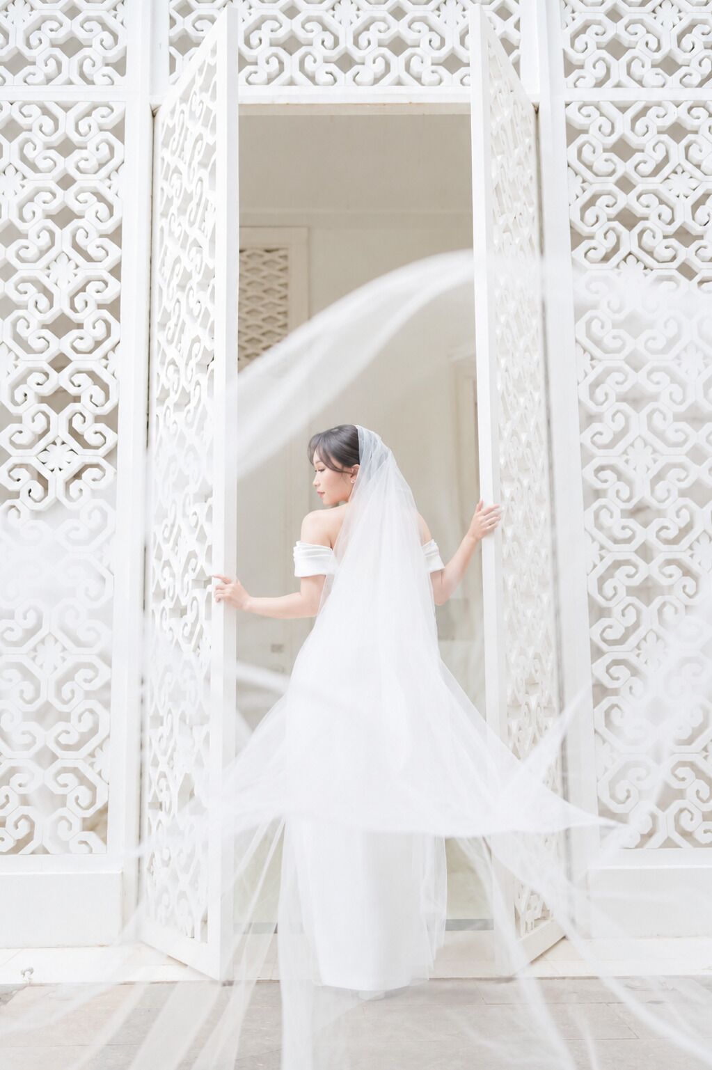 A person in a white dress standing in front of a white, intricately designed partition.