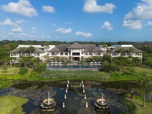 A large resort with multiple buildings, a central pool, and a pond with fountains.