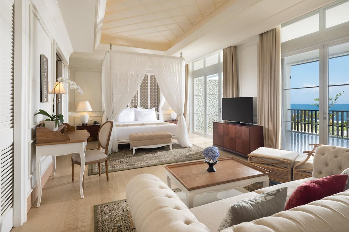 A spacious bedroom with a large bed, a TV, and a balcony with a view of the sea.