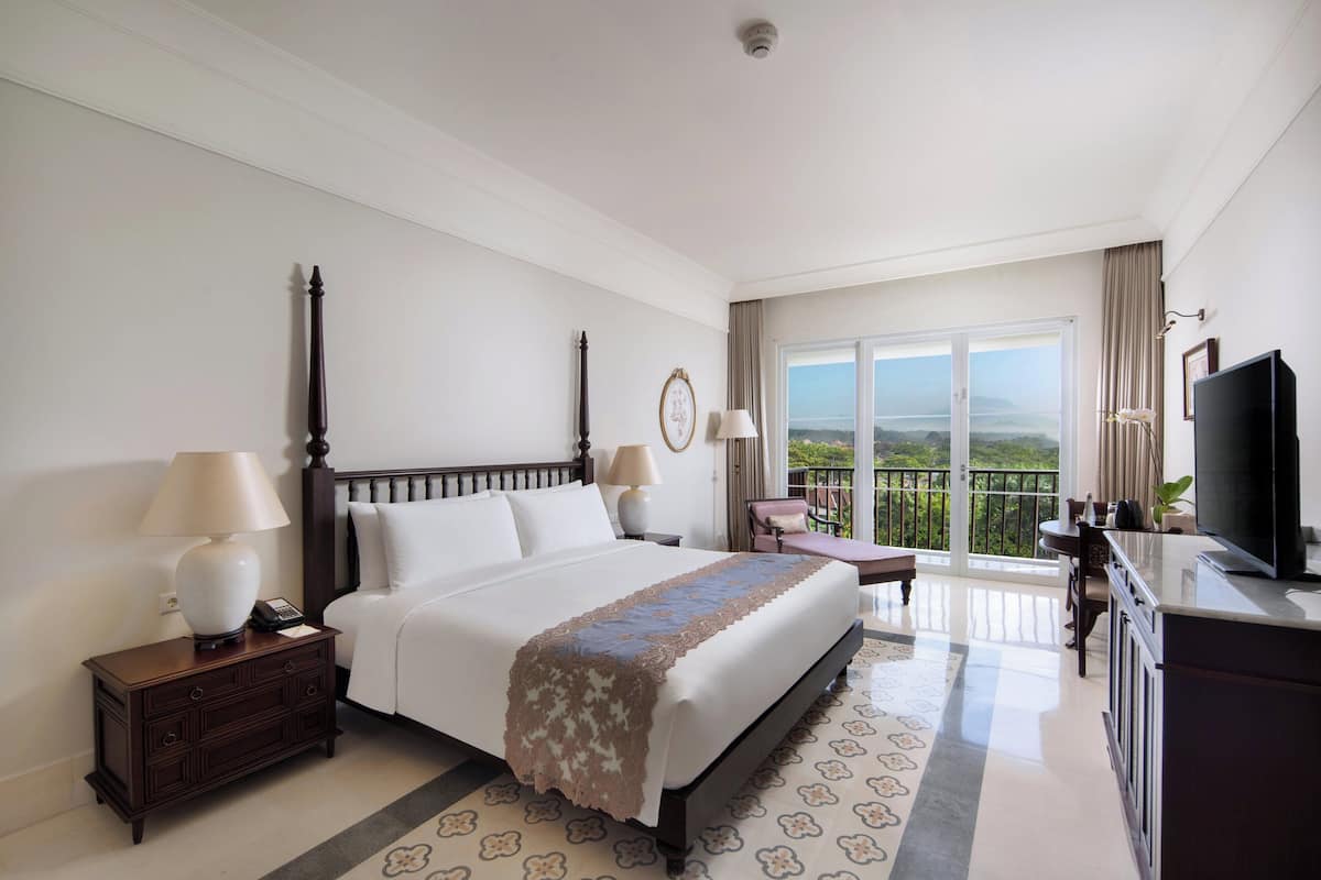 A hotel room with a large bed, a desk, a chair, a television, and a balcony with a view.