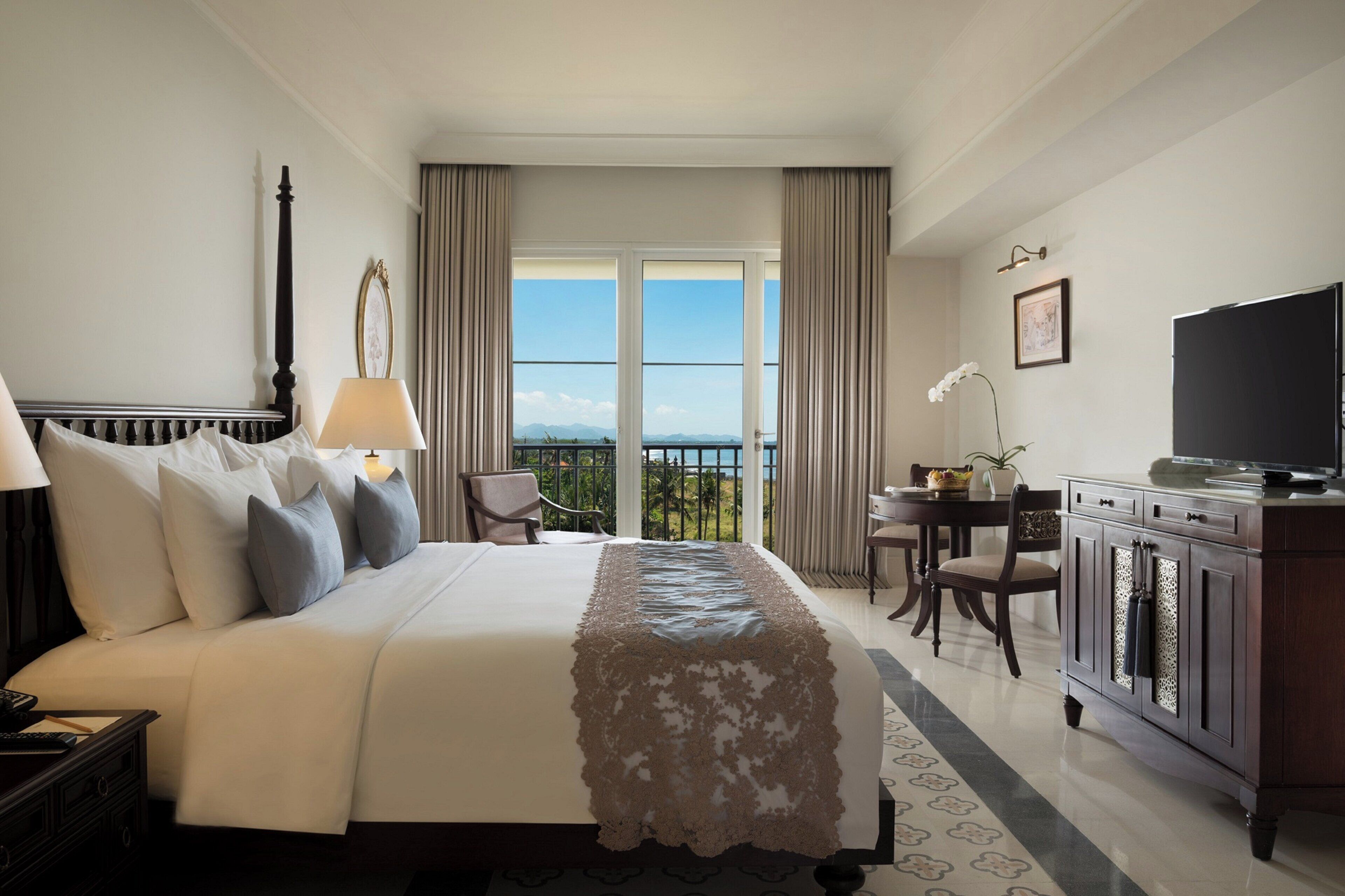 A hotel room with a large bed, a desk, a television, and a view of the outdoors.