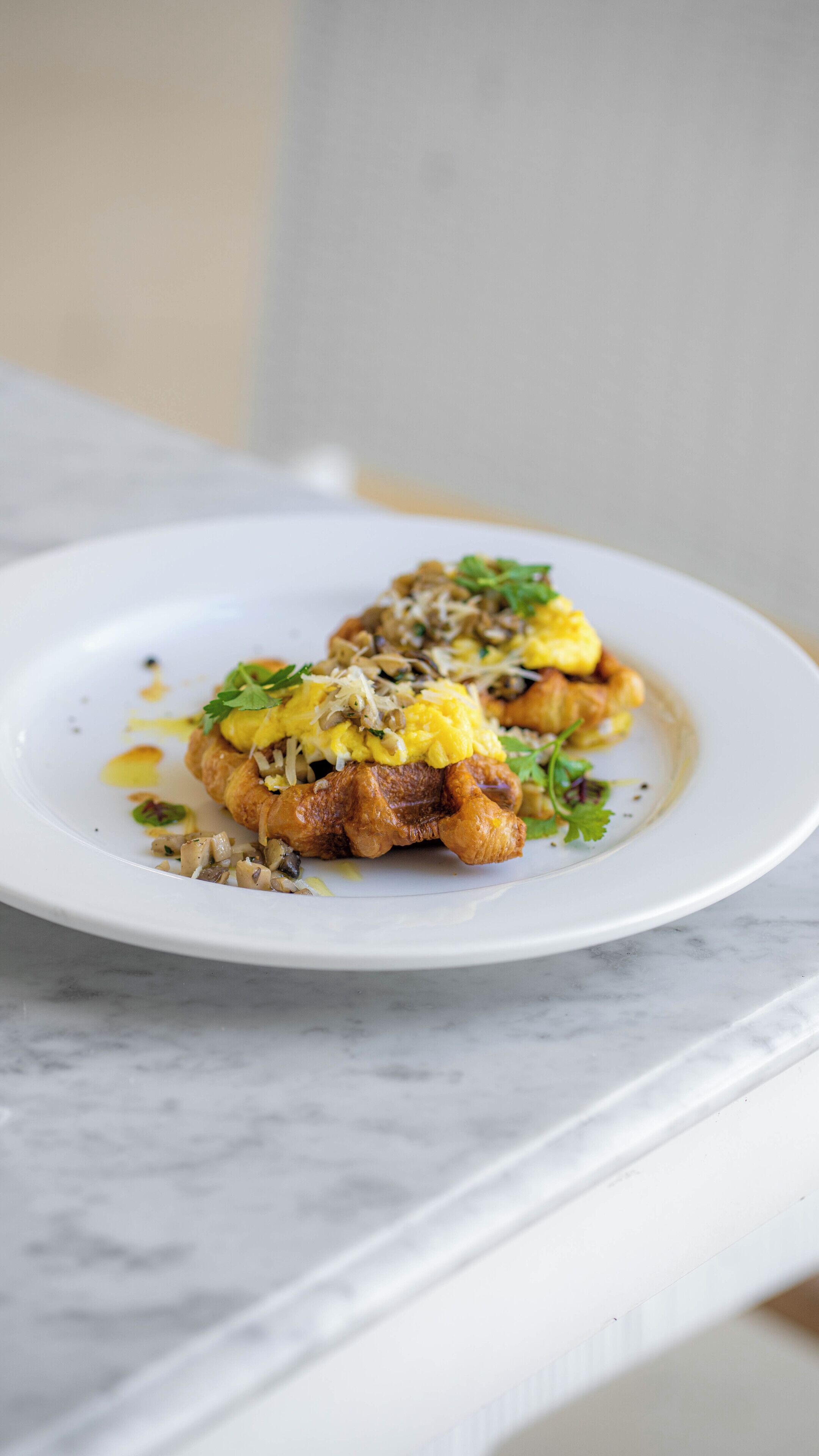 A plate of food with scrambled eggs, mushrooms, and greens on a white plate.