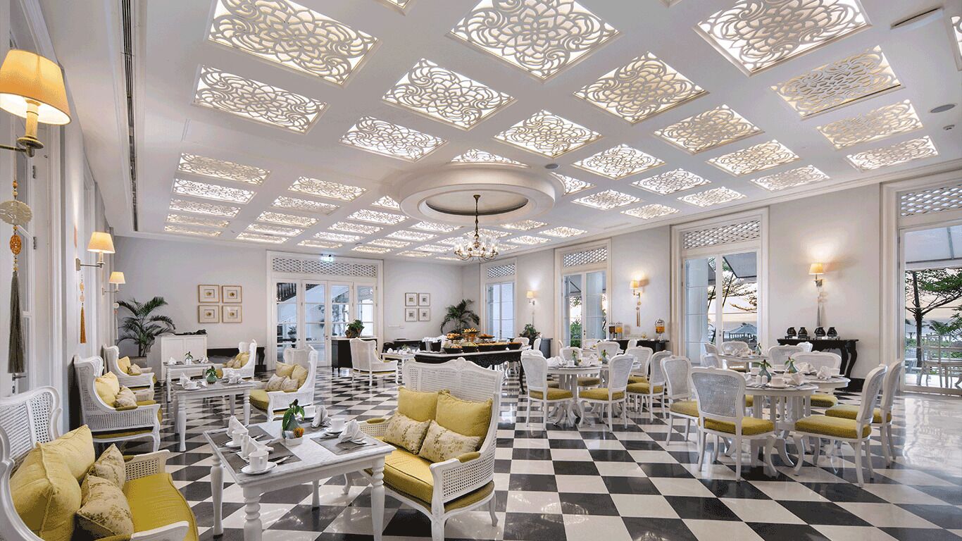 A hotel lobby with a checkered floor, white furniture, and decorative ceiling panels.