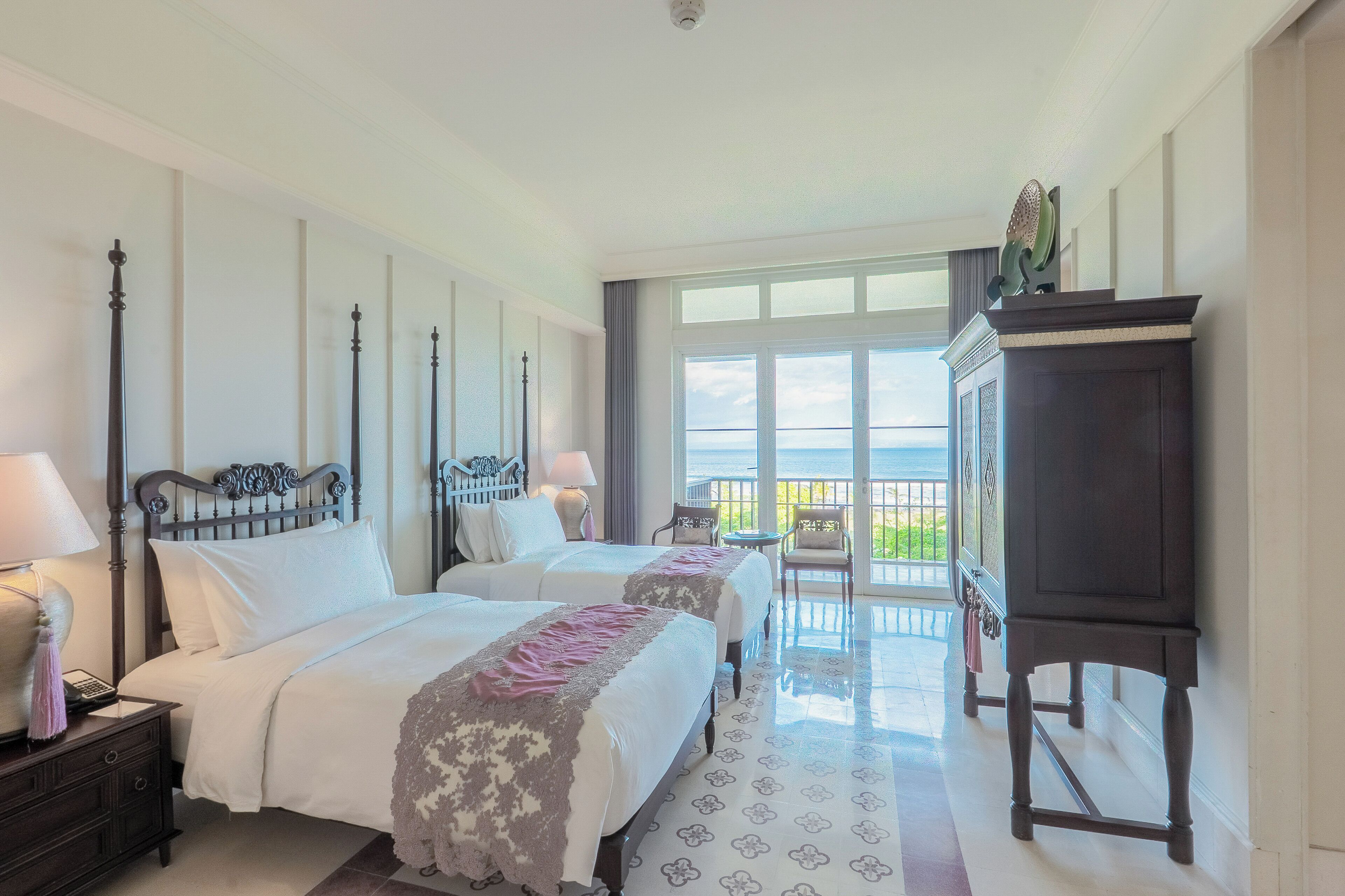 Habitación de hotel con dos camas, una mesita de noche, un aparador y un balcón con vistas.
