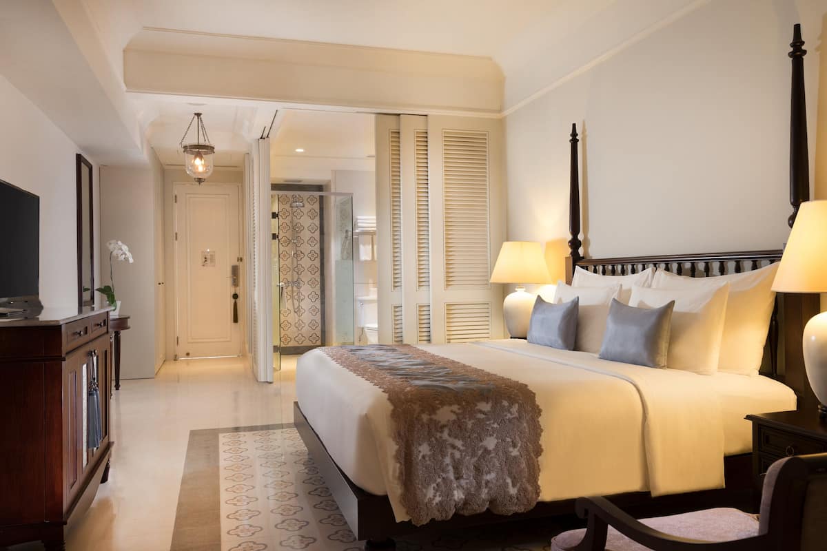 A hotel room with a large bed, bedside lamps, a TV, and a wooden nightstand.