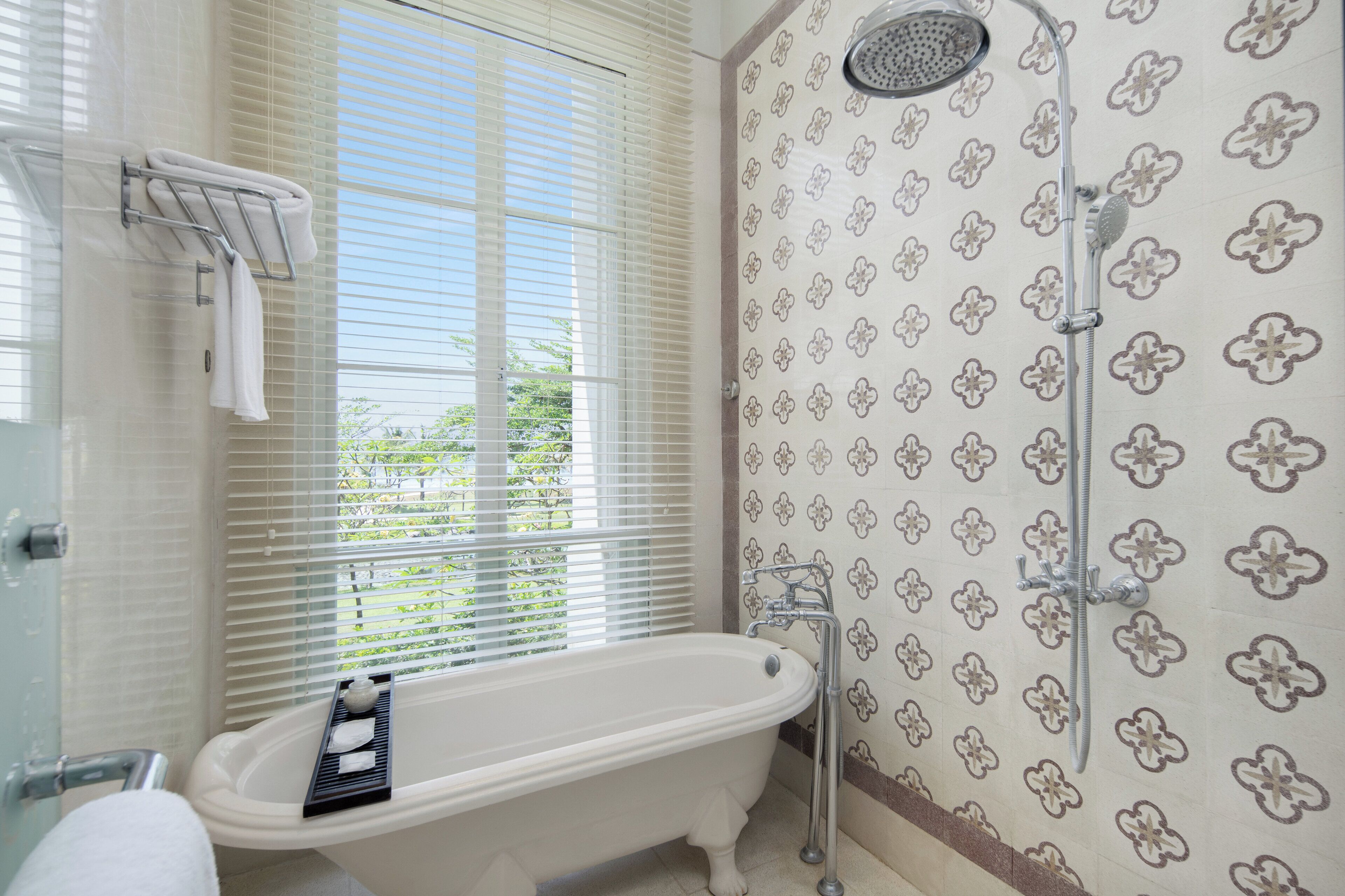 A bathroom with a freestanding bathtub, a shower with a rain showerhead, and a window with blinds.