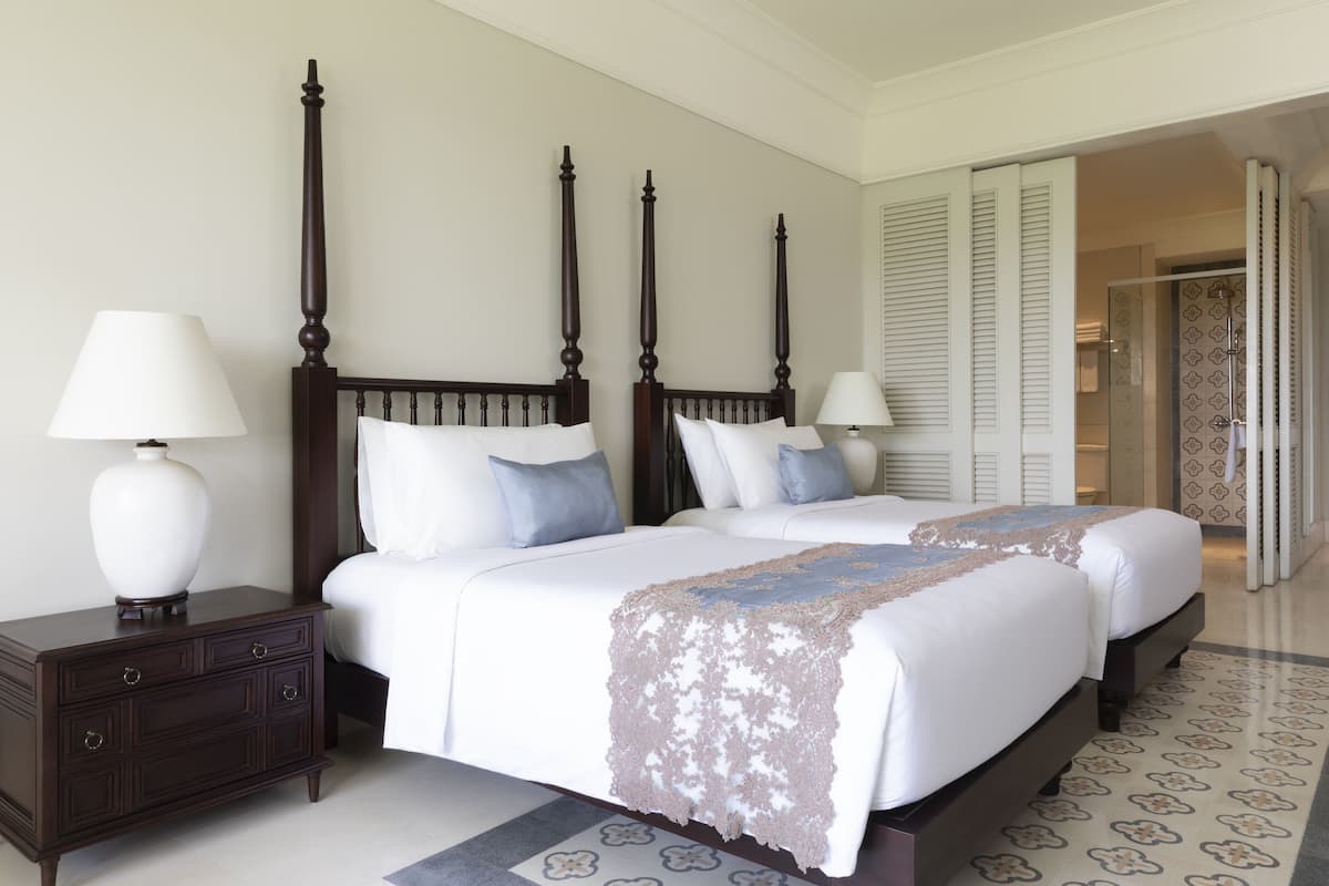 A hotel room with two beds, a nightstand, and a bathroom visible through an open door.