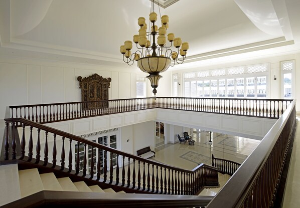 A grand staircase with a chandelier, white walls, and a balcony with a view.