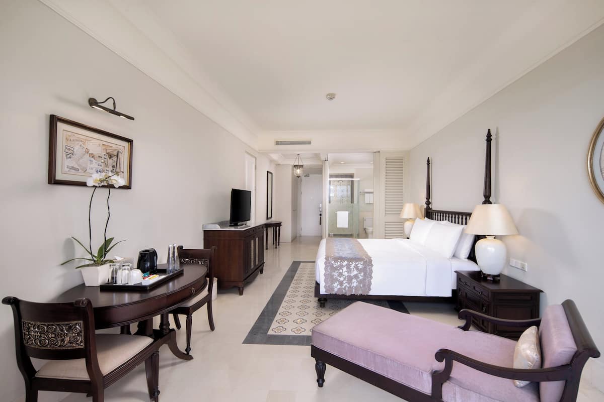 A hotel room with a bed, bedside table, lamp, desk, chair, and a dining table with chairs.