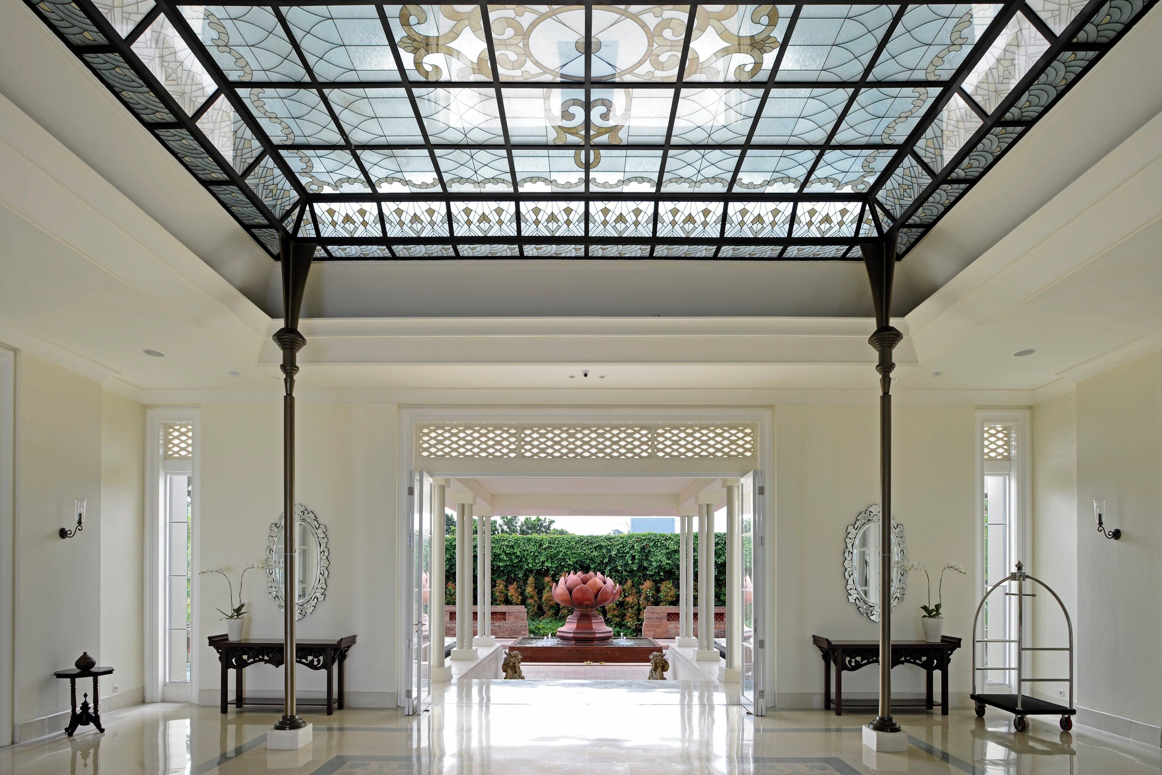 A spacious hallway with a glass ceiling, ornate columns, and a central decorative fountain.