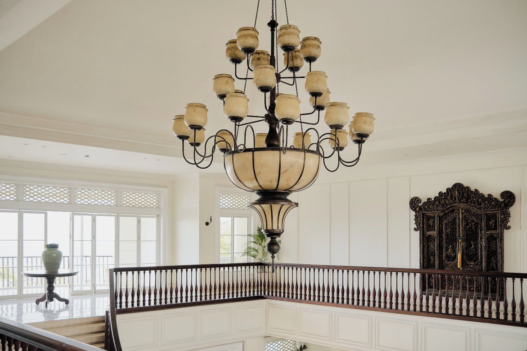 Un magnifique lustre orné de nombreuses lampes, un escalier avec une balustrade et un panneau décoratif sur le mur.