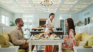 Un coin repas avec une table blanche dressée pour trois personnes, entourée de meubles en osier blanc.