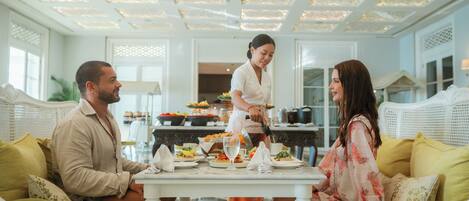 A dining area with a white table set for three, surrounded by white wicker furniture.